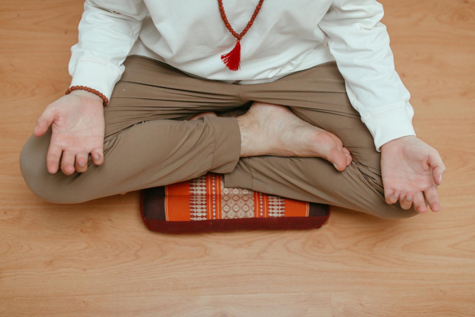 Vista aérea de un hombre meditando en casa, sentado en una pose de yoga sobre un piso de madera.